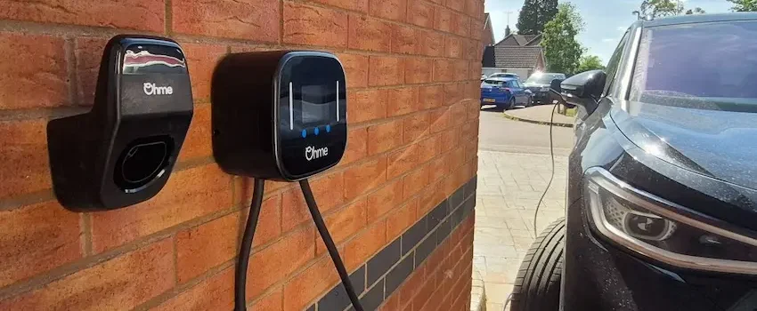 A smart EV charger installation can use load balancing to manage charging demand safely. Ohme EV charger installed on a brick wall with electric car charging on a driveway