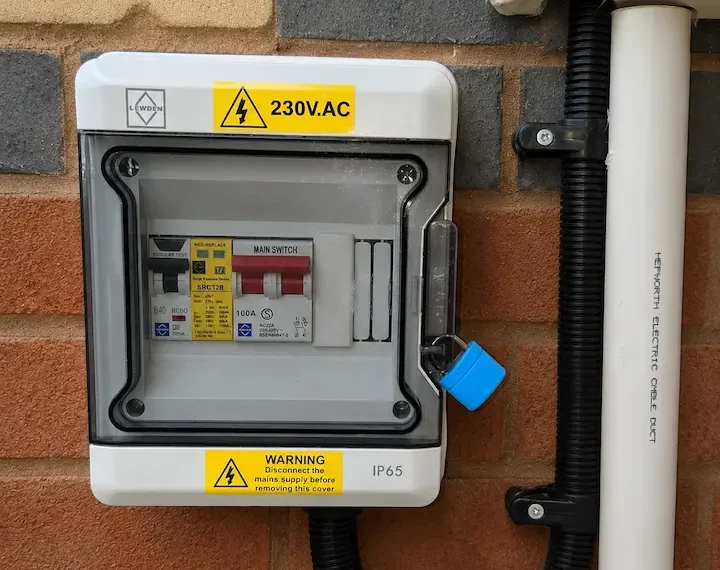 A small weatherproof EV consumer unit can sometimes be installed near the meter position where it gives a neater route to the charger. External EV consumer unit installed near a meter box for a home charger circuit.